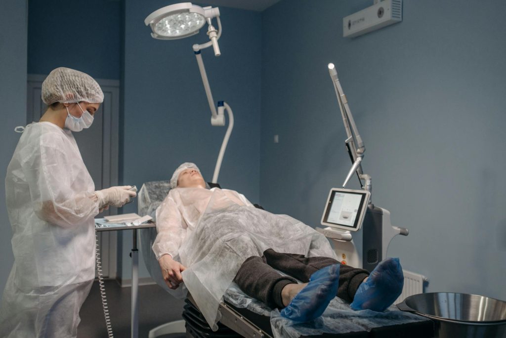 nurse with face mask standing by patient on bed in operating room